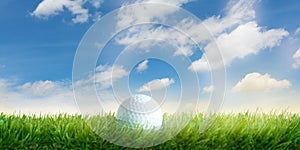 Golf ball lies in the grass before blue sky with white clouds