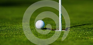 Golf ball on lip of cup on grass background. Golf hole.