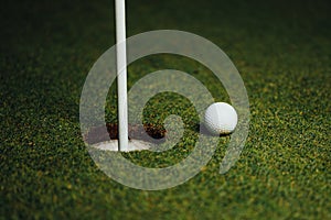 Golf ball nearby hole with pin flag, green grass background