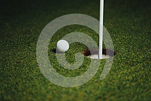 Golf ball nearby hole with pin flag, green grass background