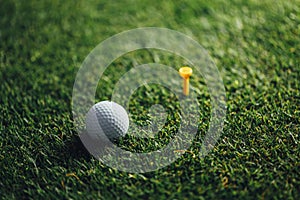 golf ball nearby yellow tee on green grass