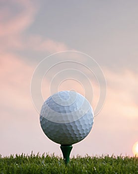 Golf ball positioned on a tee with a sunrise background capturing a serene and early morning atmosphere. photo
