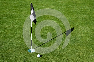 Golf ball on practice putting green next to hole and flag, sunny morning