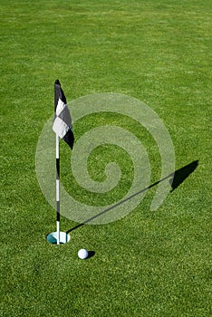 Golf ball on practice putting green next to hole and flag, sunny morning