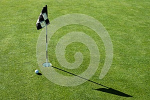 Golf ball on practice putting green next to hole and flag, sunny morning