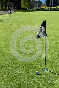 Golf ball on practice putting green next to hole and flag, sunny morning