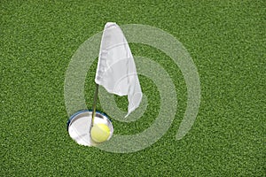 Golf ball on practice putting green next to hole and white flag.