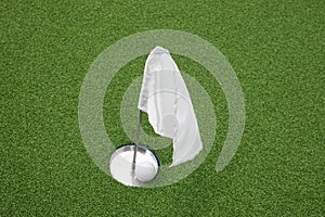 Golf ball on practice putting green next to hole and white flag.