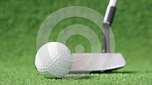 Golf ball with putter at background on green grass