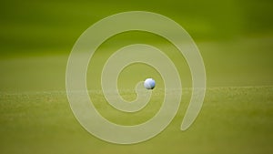 Golf ball putting on green grass near hole golf to win in game at golf course with blur background and sunlight ray