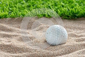 Golf ball in sand bunker near the lawn