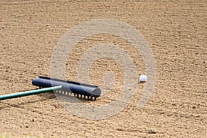 Golf ball in a sand trap with a rake