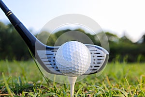 A golf ball is set on a tee in the grass and is hit with the head of a golf club