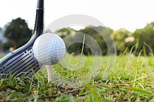 A golf ball is set on a tee in the grass and is hit with the head of a golf club.