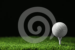 Golf ball with tee on artificial grass  black background, space for text