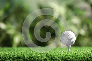 Golf ball with tee on artificial grass against blurred background