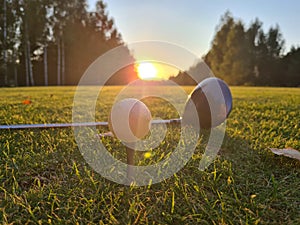 Golf ball on tee with a driver on golf course on in background of sun