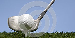 Golf ball on tee on grass with driver