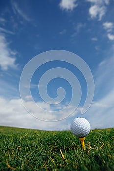 golf ball on tee, green grass and blue sky