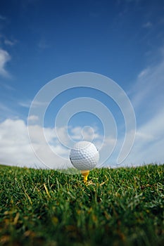 Golf ball on tee, green grass and blue sky background