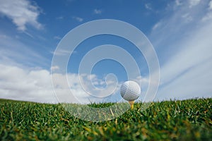 Golf ball on tee, green grass and blue sky background