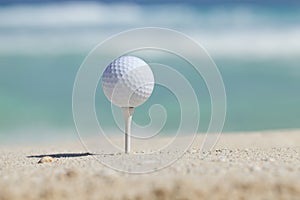 Golf ball on tee in sand beach with ocean waves behind