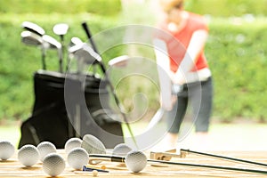 Golf balls, golf equipment, and golf club on the table on driving range with the golfer in background