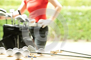 Golf balls, golf equipment, and golf club on the table on driving range with the golfer in background