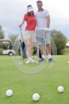 Golf balls on green with golfing couple in background