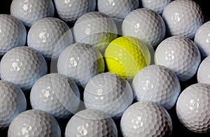 Golf balls. Single yellow ball mixed within many white balls.