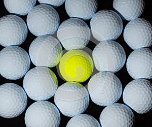 Golf balls. Single yellow ball mixed within many white balls.