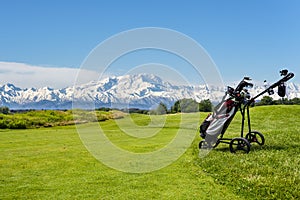 Golf cart with bag and golf clubs at the edge of the fairway of a golf course. In the background the Alps, the Monte Rosa chain,