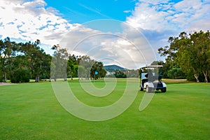 Golf cart on a golf course. Green field and cloudy blue sky. Spring landscape with grass and trees.