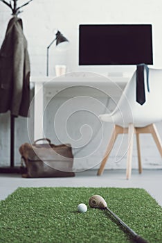golf club and ball on green grass carpet in modern workplace