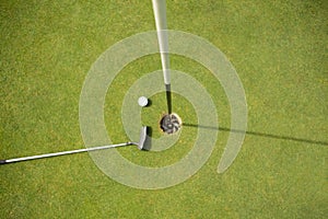 Golf club and golf ball on the putting green beside flag