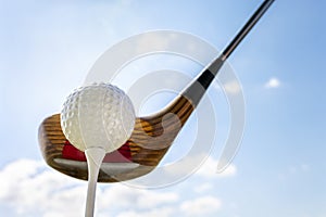 Golf club and golf ball about to tee off against a blue sky