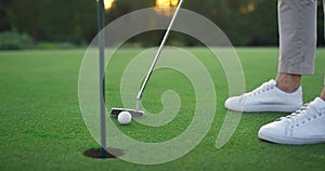 Golf club hitting ball in hole green course. Golfing player swing teeing putter.