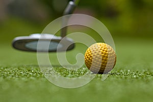 Golf club and yellow ball on artificial grass