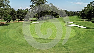 Golf course fairway and green with sand bunker hazards surrounded by trees against blue sky