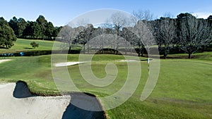 Golf course green with flag, bunkers, dam and tree lined fairway