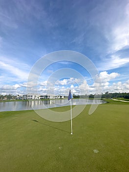 Golf course green with hole and flag with blue skies and sun. Pristine lush rich green. Southwest Florida
