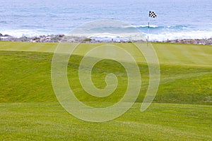 Golf course greens leading to hole by the ocean