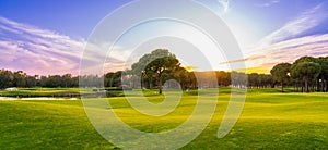 Golf course panorama at sunset with beautiful sky. Scenic panoramic view. Golf course with pine trees