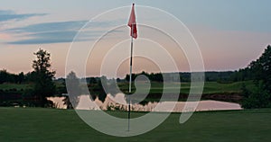 Golf course red flag in golfing hole. Flagstaff on empty green course sunset.
