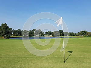 A golf course with a white flag on its hole and a pond and clear sky