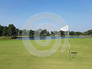 A golf course with a white flag on its hole and a pond and clear sky