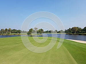 A golf course with a white flag on its hole and a pond and clear sky