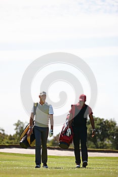 Golf is a game for gentlement. two men carrying their golf bags across a golf course.