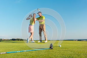 Golf instructor teaching a young woman to swing the driver club