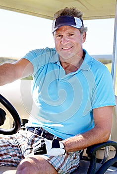 Golf is my favourite passtime. A happy mature man smiling while sitting in a golf cart.